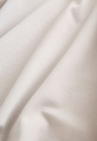 Plis de tissu doux, lisse, ivoire avec une texture subtile et des ombres douces mettant en valeur le tombé et le motif de tissage du matériau.