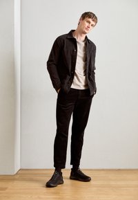 Black corduroy jacket over a light gray t-shirt, paired with black corduroy pants and dark sneakers. Simple design with buttons.