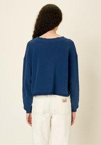 Felpa cropped blu navy con maniche lunghe, collo ampio e bordo testurizzato, abbinata a pantaloni beige a vita alta.