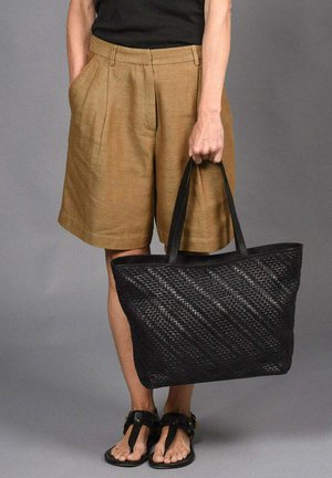 Zwarte geweven tote bag met diagonale patroon, gestructureerde vorm en stevige zwarte handvatten. Draag ik met beige shorts en sandalen.
