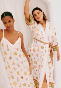 Due modelli indossano abiti leggeri e con motivi. Il modello a sinistra indossa un vestito sottoveste bianco con disegni di cuori colorati; il modello a destra indossa un kimono con stampati simili.