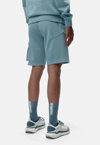 Pantalones cortos deportivos de color azul claro con un bolsillo lateral, combinados con calcetines a juego y zapatillas blancas con acentos en color agua. Textura de tela suave.