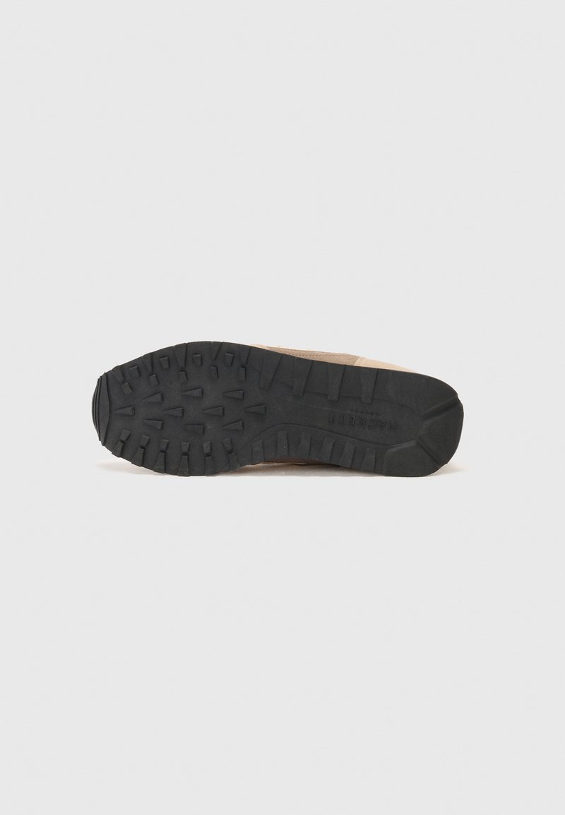 Semelle de chaussure beige unique avec un motif de pneus en caoutchouc noir vue de dessous sur fond blanc.