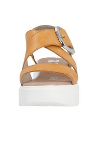 Sandale en cuir tan avec un design à large bande, une boucle en métal argenté et une semelle plateforme blanche à surface texturée.