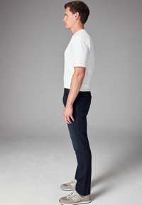 Conjunto masculino que incluye una camiseta ajustada de algodón blanco y jeans de mezclilla azul oscuro con una textura suave. Zapatillas deportivas grises con detalles blancos.