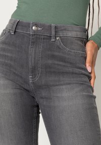 Jeans de ganga cinza com cintura alta, design de cinco bolsos e costura em contraste. O tecido tem uma textura suave e ligeiramente desgastada.