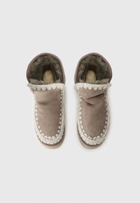 Papuci din suede maro, căptușiți cu blană moale, cu o broderie decorativă albă și un design cu călcâiul închis pentru căldură și confort.
