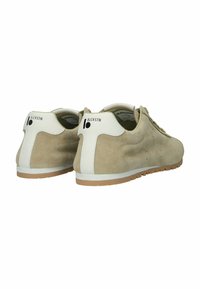 Pari beigeä mokkanahkaista tennaria, joissa on valkoiset kantapäätahrojen kohdat, kumipohjat ja musta "BLCKSTN"-logo takana, kuvattuna takaapäin.