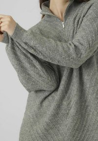 Pull-over en maille grise avec un col montant et une fermeture éclair. Présente un motif texturé et des manches surdimensionnées, offrant une coupe décontractée.