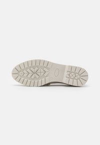 Suola di una scarpa, caratterizzata da un materiale in gomma bianca testurizzata con una trama antiscivolo, includendo design a diamante e linee per la trazione.