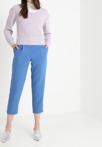 Pull en lilas tricoté avec un large col, associé à un pantalon bleu ajusté jusqu'à la cheville et des chaussures argentées à bout pointu.