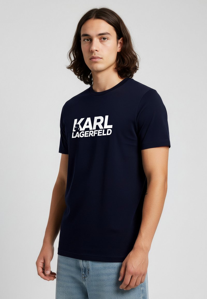 Laivaston sininen puuvillainen T-paita, jossa on lyhyet hihat ja suuri valkoinen "KARL LAGERFELD" -logo rinnassa. Sileä pinta, normaali istuvuus.