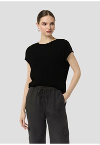 Black short-sleeve top in a soft fabric, featuring a crew neckline and subtle detail at the shoulders, paired with loose grey pants.