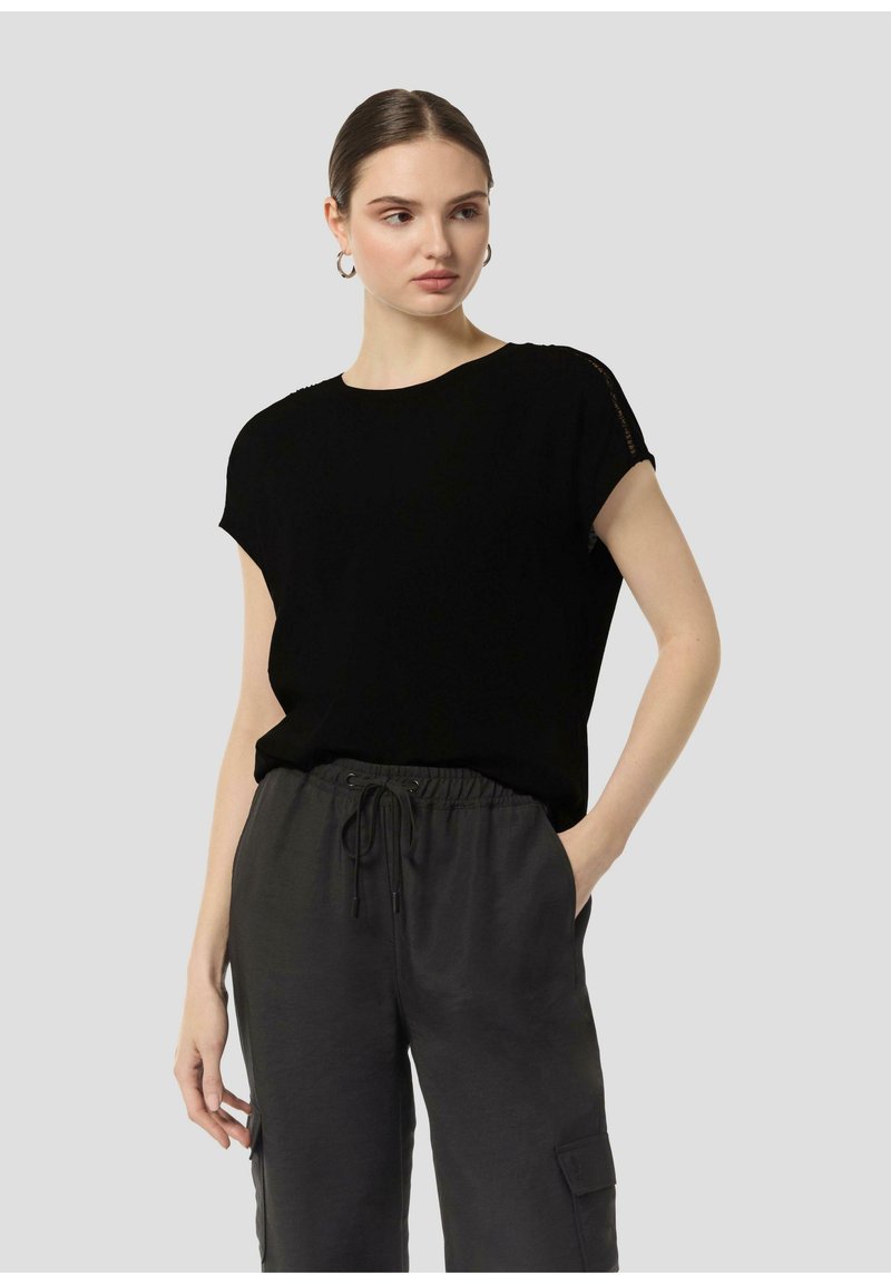 Black short-sleeve top in a soft fabric, featuring a crew neckline and subtle detail at the shoulders, paired with loose grey pants.