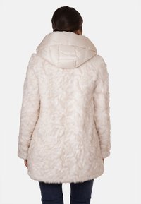 Cappotto in pelliccia sintetica color crema con un'esterno testurizzato e soffice. Presenta un ampio cappuccio imbottito per maggiore calore e una silhouette rilassata.