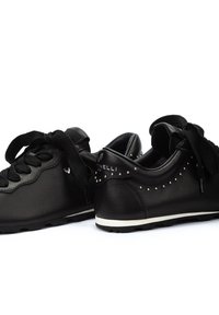 Baskets en cuir noir avec bout rond, surface texturée, lacets noirs et clous métalliques le long du talon. Semelle en caoutchouc blanche.