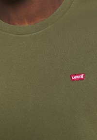 Olivově zelené tričko s krátkým rukávem vyrobené z bavlny, s malým červeným logem Levi's na levé horní části hrudi a s kulatým výstřihem.
