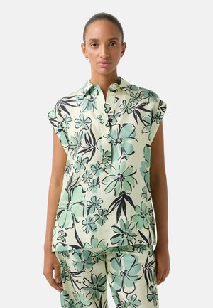 Floral print blouse in light green, featuring short rolled sleeves, a collar, and a buttoned placket. Smooth fabric with black accents.