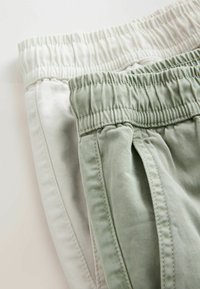 Deux pantalons à taille élastique, un beige clair et un vert clair, pliés avec des coutures visibles et des poches latérales.