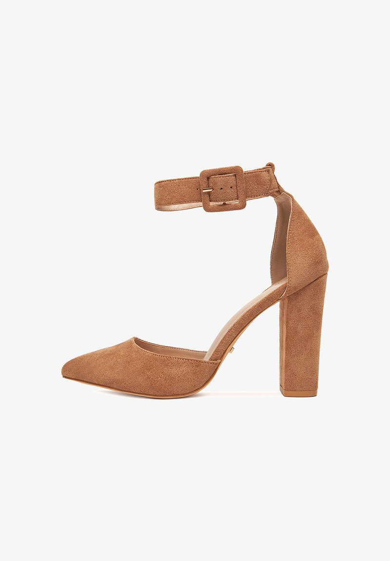 Zapato de tacón alto de ante marrón con punta puntiaguda, correa en el tobillo, hebilla cuadrada y tacón grueso. Forro interior suave para mayor comodidad.