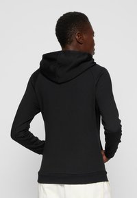 Svart hettegenser med en avslappet passform, justerbar hette med snor og mansjetterte ermer. Stoffet har en jevn tekstur med minimal sømdetaljer.