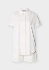 Chemise blanche à manches courtes avec boutons et bords festonnés, accompagnée d'un short blanc assorti sur un fond uni.