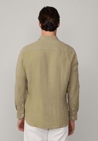 Camicia a maniche lunghe con colletto di un verde oliva chiaro, realizzata in un tessuto strutturato con polsini con bottone, vista da dietro.