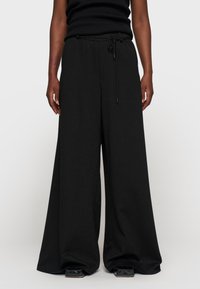 Pantalones anchos negros con cintura ajustable mediante cordón. Confeccionados en una tela texturizada con sutiles rayas verticales.