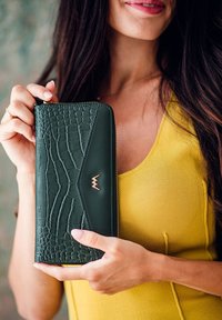 Green wallet with a textured crocodile pattern, zip closure, and gold accent logo. Smooth leather edges and rectangular shape.