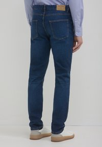 Jeans in denim blu scuro con una vestibilità slim, dotati di una patch in pelle sulla vita e due tasche posteriori. Texture liscia con leggero stretching.