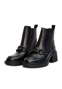 Paire de bottines en cuir noir avec talons épais et détail décoratif en chaîne sur le devant, sur fond blanc.