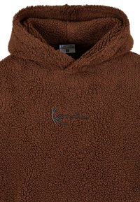 Felpa con cappuccio marrone in pile con una finitura testurizzata e soffice. Presenta un cappuccio e un logo ricamato in nero sul davanti.