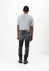 Vaaleanharmaa lyhythihainen paita, tummanharmaat slim fit -farkut, joissa on haalistunut vaikutelma, ja tummat kengät. Farkuissa on etiketti takana.