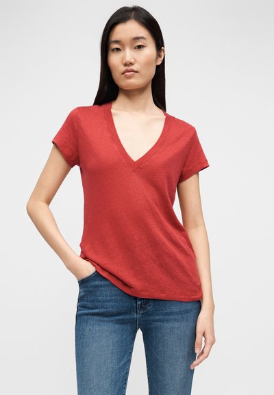 T-shirt vermelha com decote em V, mangas curtas, tecido leve, ajuste ligeiramente folgado, combinada com jeans azul. Textura suave, design minimalista.