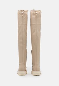 Knæhøje, beige faux læderstøvler med en glat overflade, snørebåndsdetaljer øverst og kontrastfarvede cremede gummisåler.