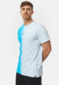 Camiseta azul claro con un diseño degradado que se desvanece a un azul brillante. Tiene un cuello redondo y un pequeño logo negro en el pecho. Mangas cortas.