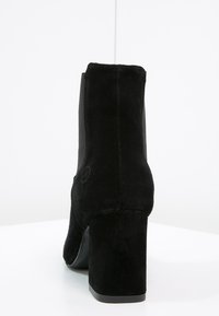 Bottines en suede noir avec un talon bloc, dotées de panneaux latéraux élastiques et d'une finition lisse, offrant un design épuré et minimaliste.