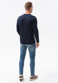 Maglietta blu navy a maniche lunghe con scollo a giro, abbinata a jeans skinny blu chiaro e sneakers multicolori, vista da dietro.