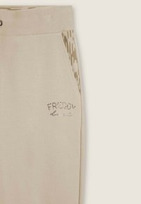 Pantalones de chándal beige con una textura suave, que cuentan con un panel lateral estampado y un texto brillante "FREDDY" en strass en la parte frontal.