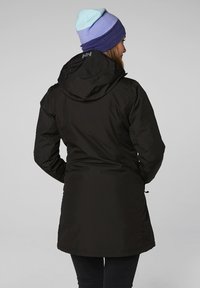 Černá venkovní bunda s přiléhavým střihem, kapucí a jemnými švy. Nositá s barevnou pletenou čepicí.