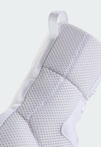 Bílé síťované tenisky s texturovaným svrškem, vyšitými detaily a zadním poutkem pro snadné obouvání. Lehký design s prodyšným materiálem.