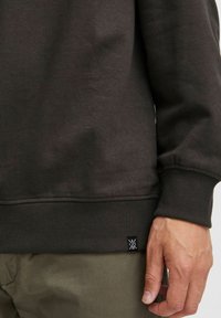Dunkelgrauer Sweatshirt mit gerippten Bündchen und Saum, ausgestattet mit einem kleinen Logotag an der unteren Seite. Weiches Material, lässiger Schnitt.
