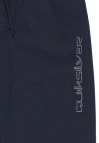 Mørkeblå joggerbukser lavet af blødt stof, med et sølv Quiksilver-logo langs den ene side. Inkluderer justerbar snøre i taljen.