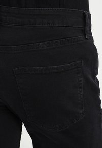 Jeans de denim negro con un bolsillo trasero, textura suave y sutiles detalles de costura. Vista en primer plano del diseño trasero.