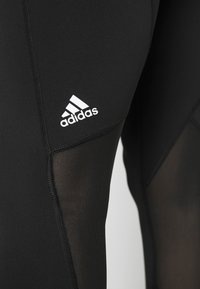 Svarta träningsleggings med nätpaneler, elastiskt midjeband och vitt Adidas-logotyp. Har flatlocksömmar för komfort och flexibilitet.