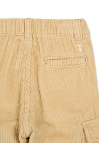Beżowe spodnie sztruksowe mają pionowe prążki, elastyczny pas i tylną kieszeń naszywaną z subtelnym haftem.