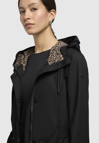 Schwarze wasserdichte Jacke mit einem Leopardenmuster-Futter, ausgestattet mit einer Kapuze, Knöpfen, Kordelzug und seitlichen Taschen. Glatte Textur.