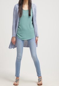 Ljusblå stickad cardigan över en mintgrön topp, matchad med ljusblå skinny jeans och sandaler med silverdekorationer.