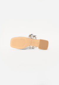 Sandalo bianco con tacco a spillo, punta quadrata, finitura lucida, cinturini regolabili e un fiocco decorativo sul lato. Suola in gomma con scanalature per la presa.