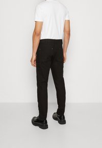 Pantalones cargo negros con múltiples bolsillos, corte ajustado y una tela duradera. Se llevan con una camiseta blanca básica y zapatos negros.